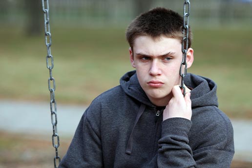 Teenage boy sat on a swing looking despondant